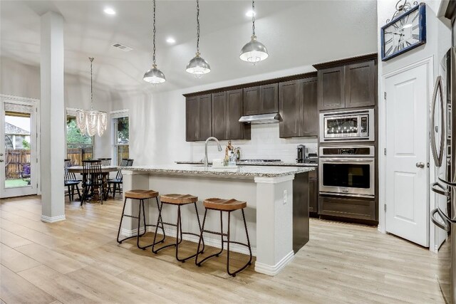 kitchen featuring stainless steel appliances, under cabinet range hood, a sink, backsplash, and a breakfast bar