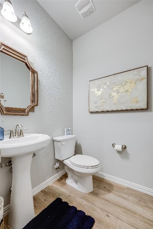 half bathroom with baseboards, wood finished floors, toilet, a textured wall, and a sink