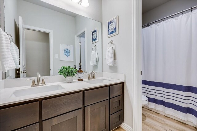bathroom featuring double vanity, wood finished floors, toilet, and a shower with shower curtain