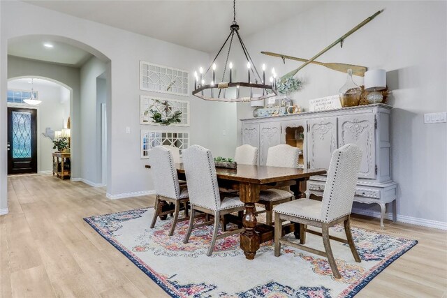 dining space featuring arched walkways, light wood-type flooring, a chandelier, and baseboards