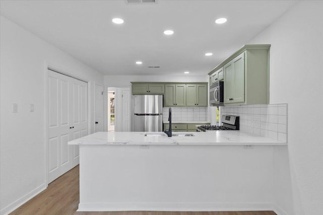 2310 Raintree Path, Round Rock, TX 78664 - kitchen featuring green cabinetry, stainless steel appliances, wood finished floors, a peninsula, and backsplash