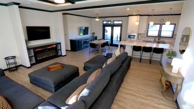 living area featuring crown molding, light wood finished floors, french doors, and ceiling fan
