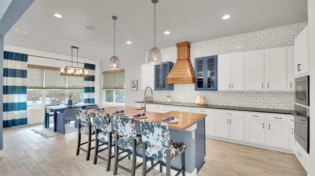 1506 Fox Sparrow Trl, Cedar Park, TX 78613 - kitchen with stainless steel appliances, custom range hood, light wood-type flooring, backsplash, and glass insert cabinets