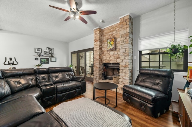 living room with ceiling fan, healthy amount of natural light, a stone fireplace, a textured ceiling, and wood finished floors