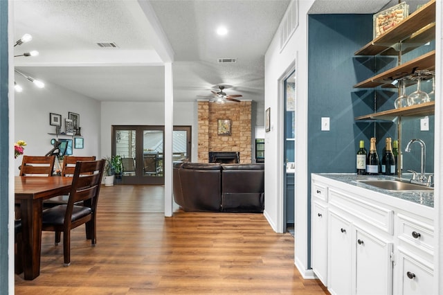 indoor bar featuring a stone fireplace, a ceiling fan, light wood-type flooring, a textured ceiling, and beam ceiling