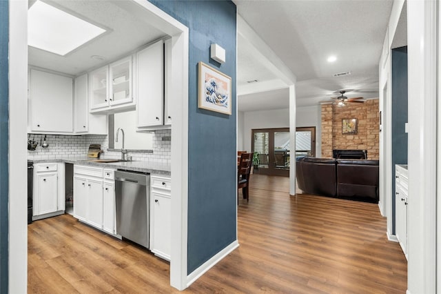 kitchen with stainless steel dishwasher, a sink, a ceiling fan, a stone fireplace, and white cabinetry
