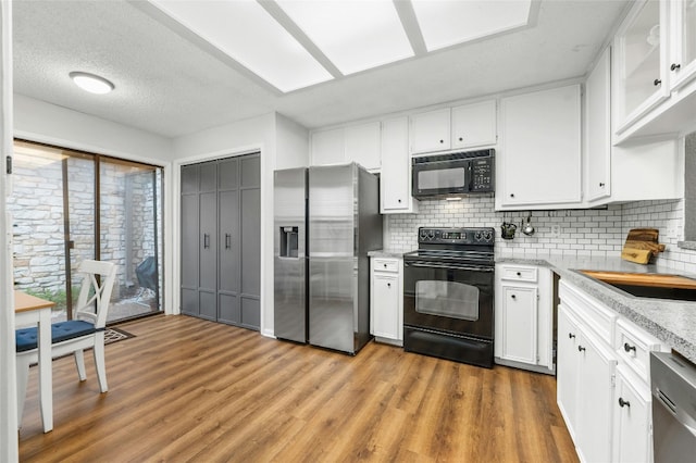 kitchen with black appliances, white cabinetry, tasteful backsplash, and light wood-type flooring