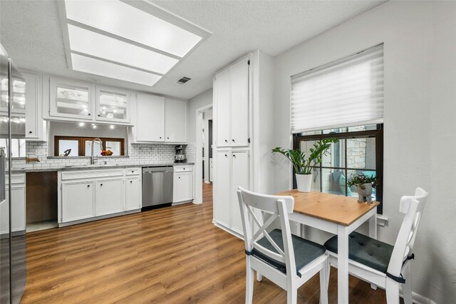 kitchen with stainless steel dishwasher, a sink, tasteful backsplash, light wood-type flooring, and a textured ceiling