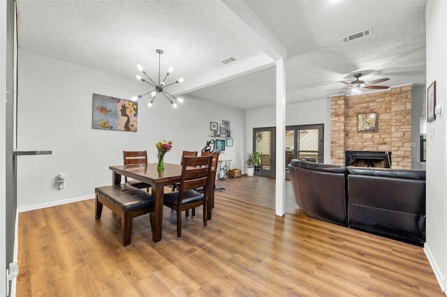 dining area with a textured ceiling, light wood-style flooring, a stone fireplace, and ceiling fan