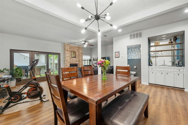 dining space featuring a stone fireplace, a chandelier, light wood-type flooring, a ceiling fan, and recessed lighting