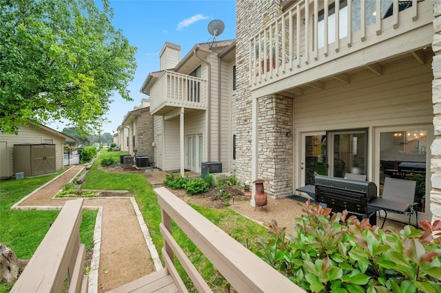 view of green lawn featuring a balcony, an outdoor structure, central AC unit, and a storage shed