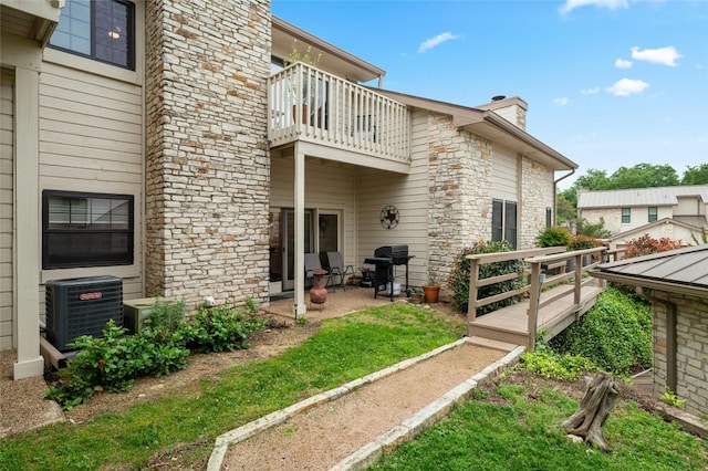 back of property featuring a balcony, cooling unit, a chimney, a patio area, and stone siding