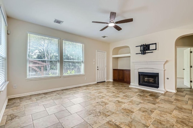 409 S Frontier Ln, Cedar Park, TX 78613 - unfurnished living room featuring arched walkways, built in shelves, a ceiling fan, a fireplace with raised hearth, and baseboards