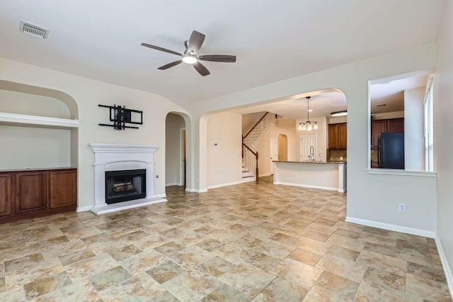 409 S Frontier Ln, Cedar Park, TX 78613 - unfurnished living room with arched walkways, a ceiling fan, a sink, a fireplace with raised hearth, and stairway