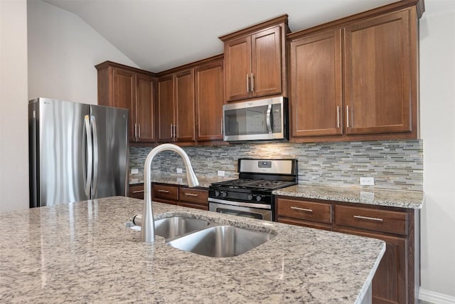 kitchen with stainless steel appliances, a sink, backsplash, light stone countertops, and vaulted ceiling