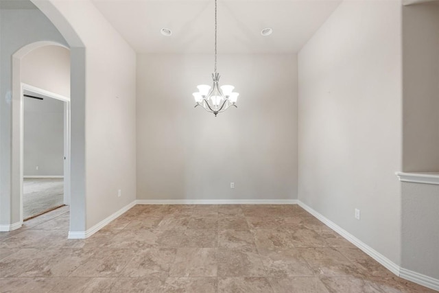 empty room with arched walkways, a chandelier, baseboards, and light stone finish flooring
