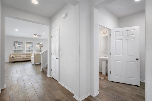 corridor with wood finished floors, recessed lighting, a sink, stairway, and baseboards