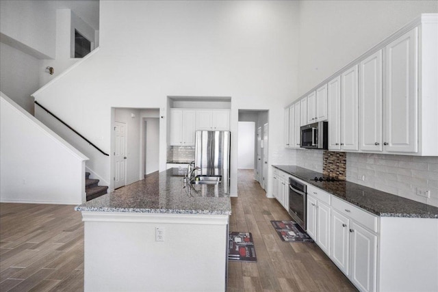 kitchen featuring stainless steel appliances, a sink, a towering ceiling, dark wood finished floors, and white cabinets