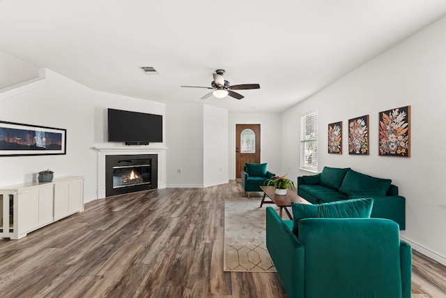 living room featuring wood finished floors, ceiling fan, a tiled fireplace, and baseboards