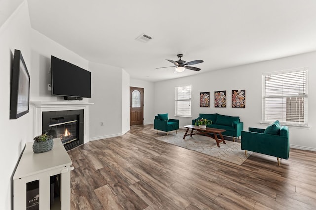living room featuring wood finished floors, a ceiling fan, a tile fireplace, and baseboards