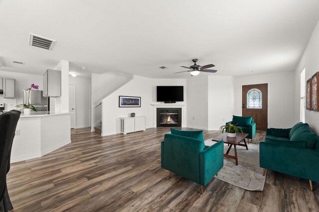 living room featuring ceiling fan, wood finished floors, a glass covered fireplace, and stairway