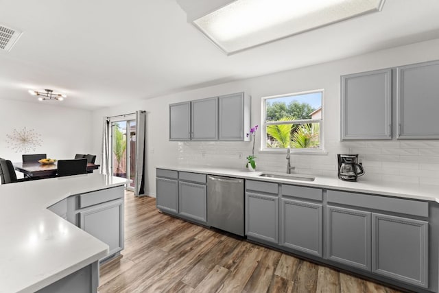 kitchen featuring stainless steel dishwasher, gray cabinets, a sink, and decorative backsplash