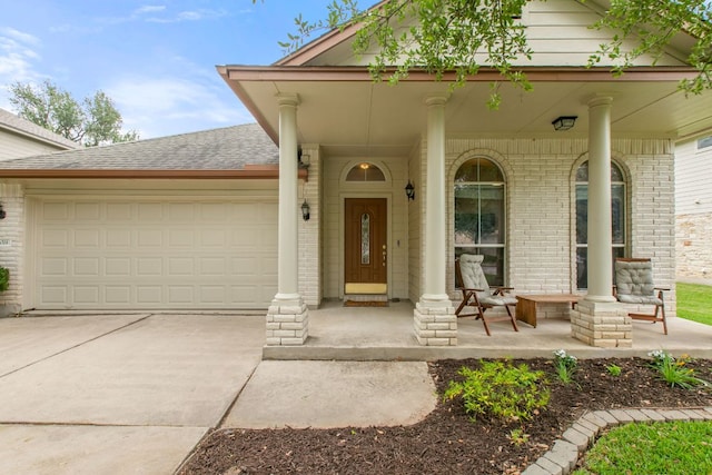property entrance featuring covered porch, brick siding, an attached garage, concrete driveway, and roof with shingles