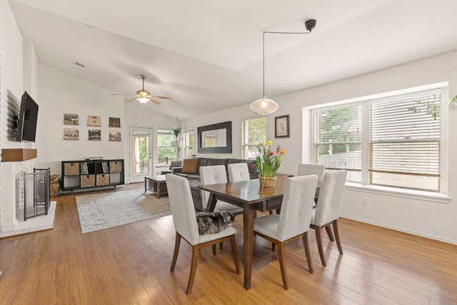 dining space featuring wood-type flooring, lofted ceiling, a ceiling fan, a fireplace, and baseboards