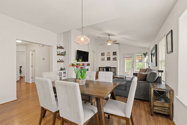 dining area with light wood-style floors, ceiling fan, vaulted ceiling, and arched walkways