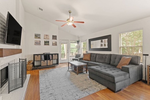 living room with lofted ceiling, ceiling fan, a fireplace with raised hearth, and light wood-style floors
