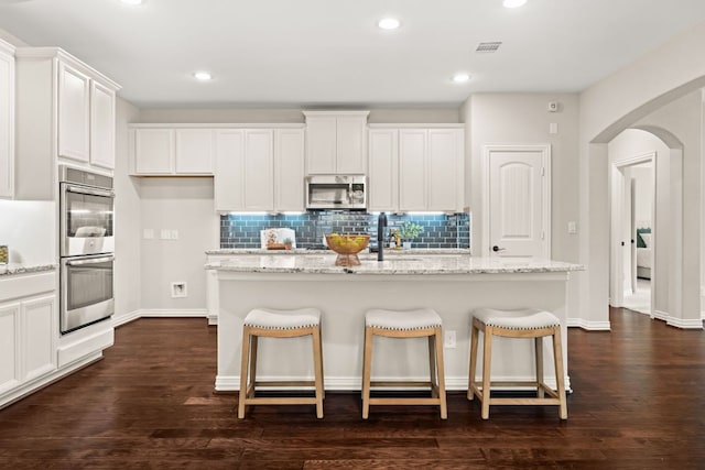 kitchen with appliances with stainless steel finishes, arched walkways, tasteful backsplash, light stone countertops, and white cabinets