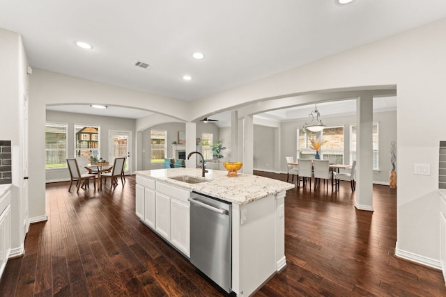kitchen featuring stainless steel dishwasher, a sink, arched walkways, an island with sink, and white cabinetry