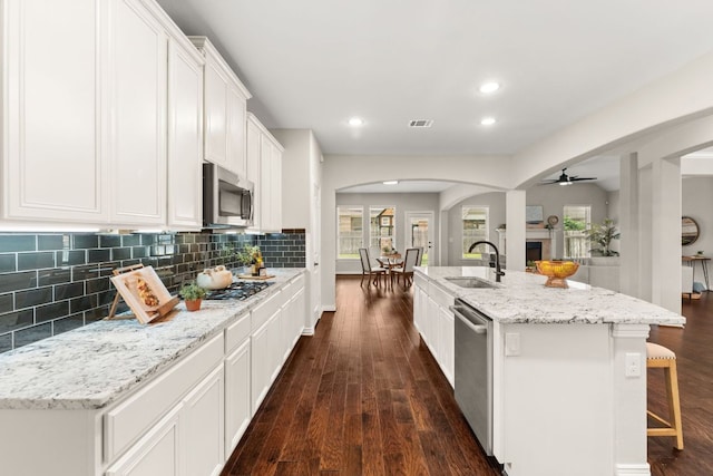 kitchen with a sink, appliances with stainless steel finishes, dark wood-style flooring, arched walkways, and recessed lighting