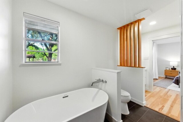 full bath featuring tile patterned flooring, a freestanding tub, toilet, and baseboards