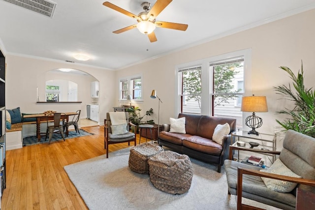 living room with arched walkways, light wood finished floors, ceiling fan, and ornamental molding