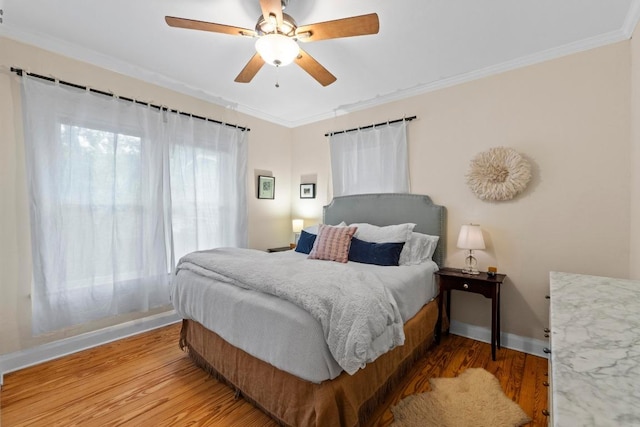 bedroom featuring light wood-type flooring, baseboards, crown molding, and a ceiling fan