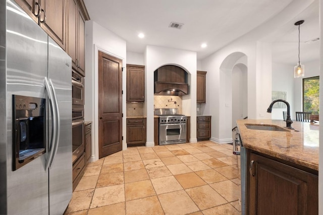 kitchen featuring appliances with stainless steel finishes, a sink, tasteful backsplash, light stone countertops, and hanging light fixtures