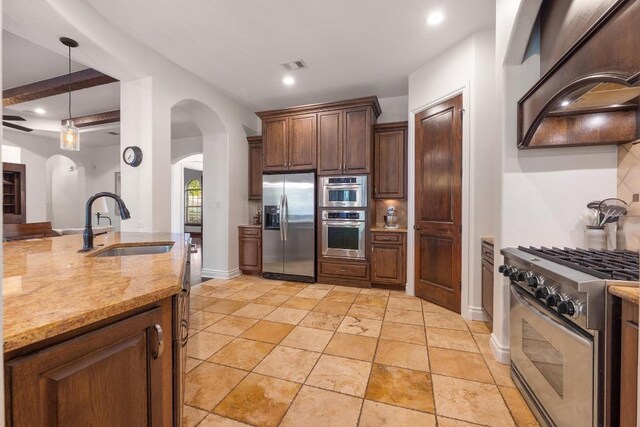 4105 Michael Neill Dr, Austin, TX 78730 - kitchen with appliances with stainless steel finishes, a sink, wall chimney range hood, arched walkways, and light stone countertops