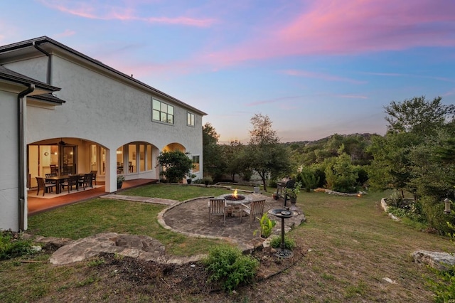 back of property at dusk featuring a fire pit, a patio area, a yard, stucco siding, and french doors