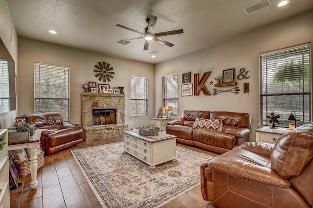 115 Loblolly Ln, Bastrop, TX 78602 - living room featuring ceiling fan, healthy amount of natural light, a stone fireplace, wood finished floors, and a textured ceiling