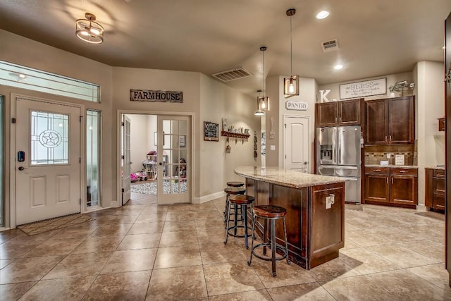 115 Loblolly Ln, Bastrop, TX 78602 - kitchen with stainless steel fridge, a breakfast bar area, light stone countertops, baseboards, and backsplash