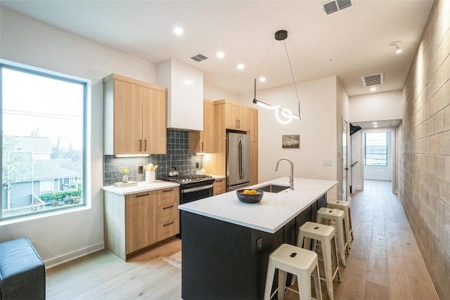 700 Denson Dr Unit 1101, Austin, TX 78752 - kitchen with stainless steel appliances, light brown cabinetry, a sink, a breakfast bar area, and light wood-type flooring