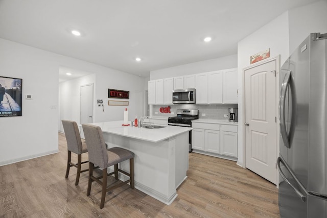 kitchen with stainless steel appliances, a sink, tasteful backsplash, white cabinets, and a breakfast bar area