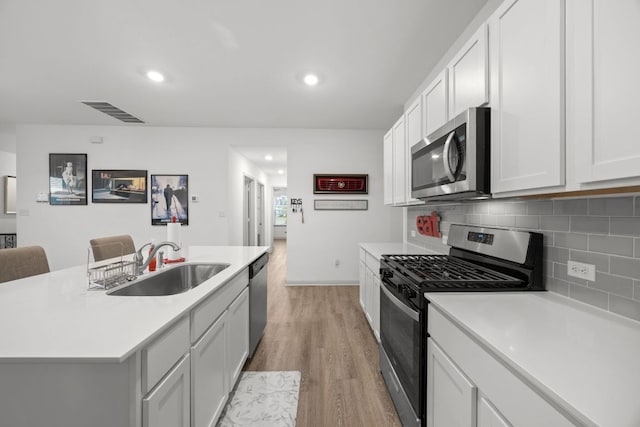 kitchen featuring stainless steel appliances, a sink, light wood finished floors, tasteful backsplash, and light countertops