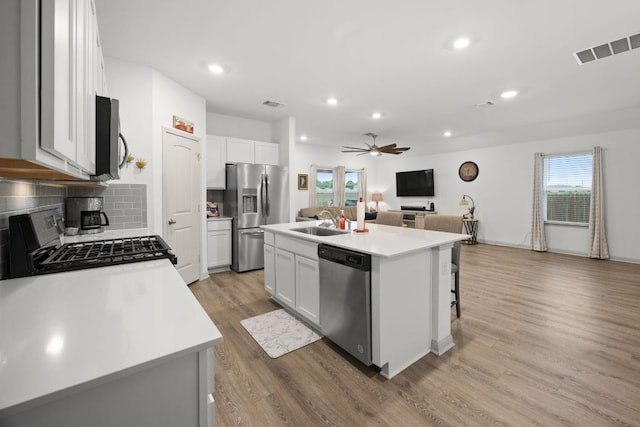 kitchen featuring stainless steel appliances, ceiling fan, light wood-style floors, a kitchen island with sink, and a sink