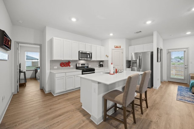 kitchen featuring stainless steel appliances, tasteful backsplash, light countertops, a kitchen bar, and white cabinetry