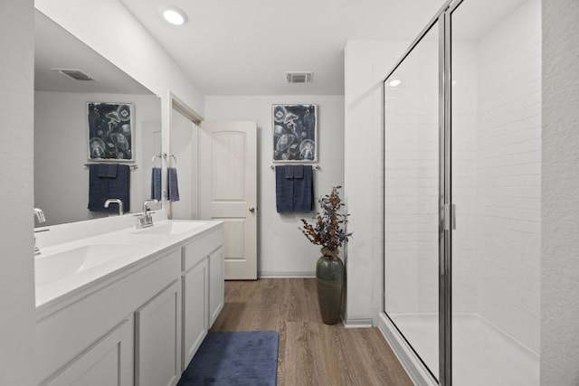 bathroom with wood finished floors, a stall shower, and double vanity