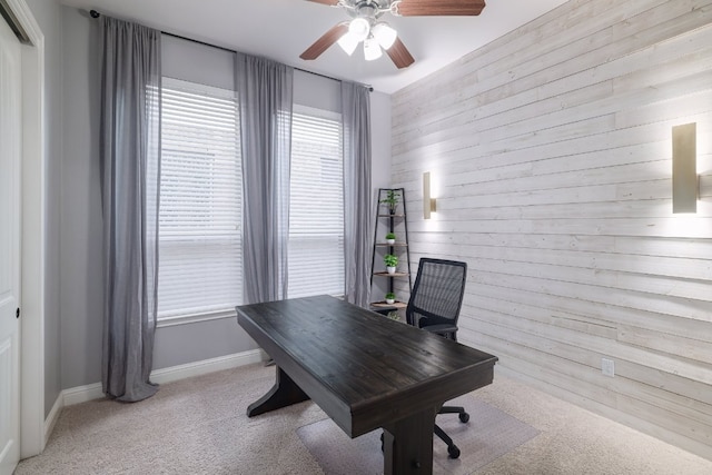 office featuring wooden walls, ceiling fan, light carpet, and baseboards