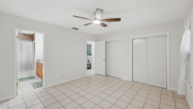 unfurnished bedroom featuring two closets, ensuite bathroom, a ceiling fan, baseboards, and light tile patterned floors