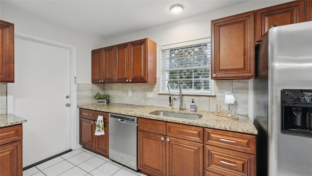 kitchen with stainless steel appliances, a sink, tasteful backsplash, light stone countertops, and light tile patterned floors